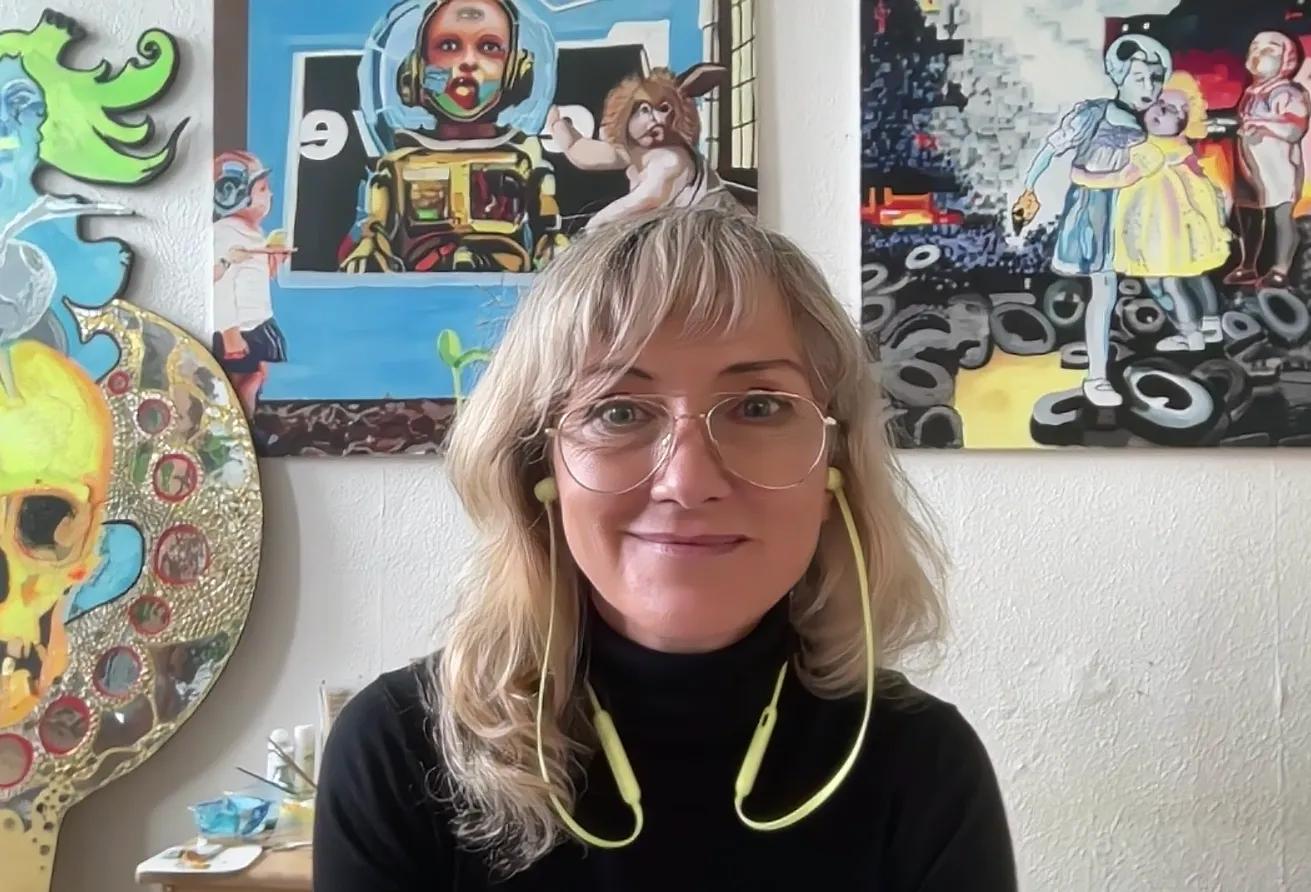 Photo of CW Stubbs on a video call with her artwork on the wall behind