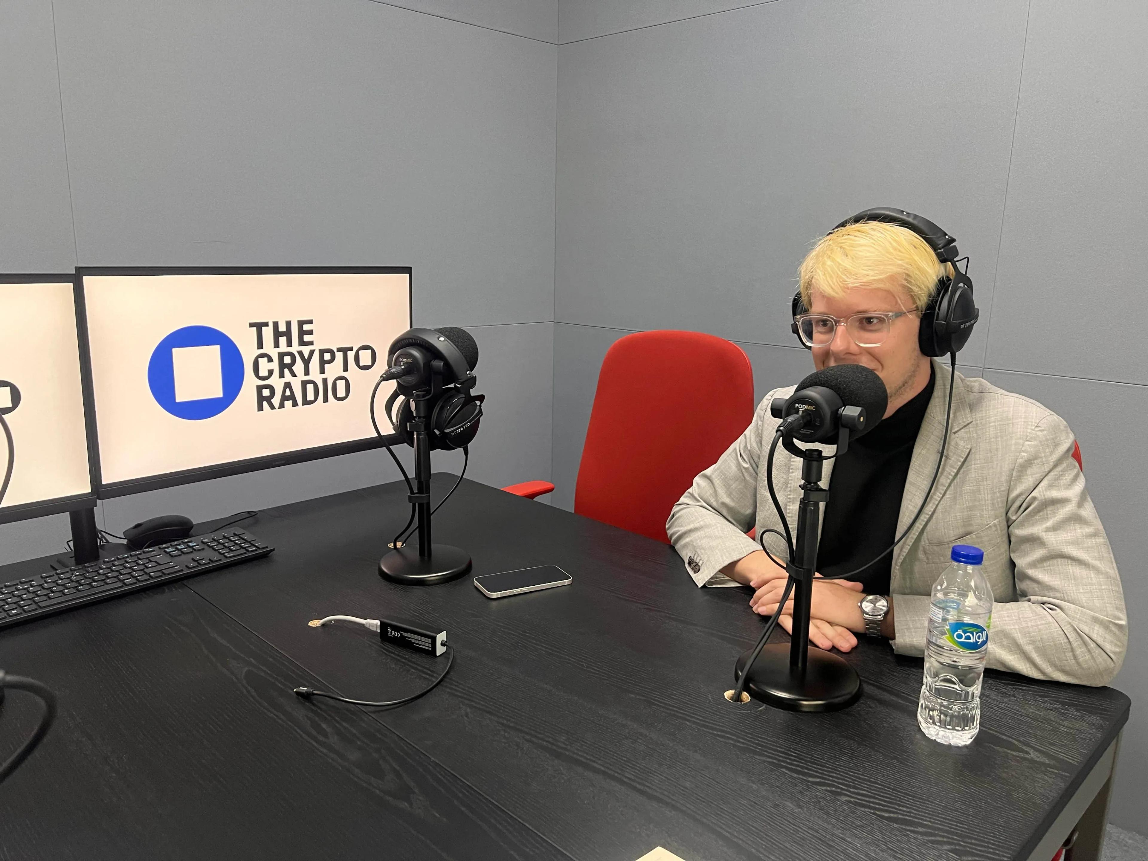 Thierry Bouchard, Erik Finman, and Justin Harper sitting on a sofa under a The Crypto Radio sign