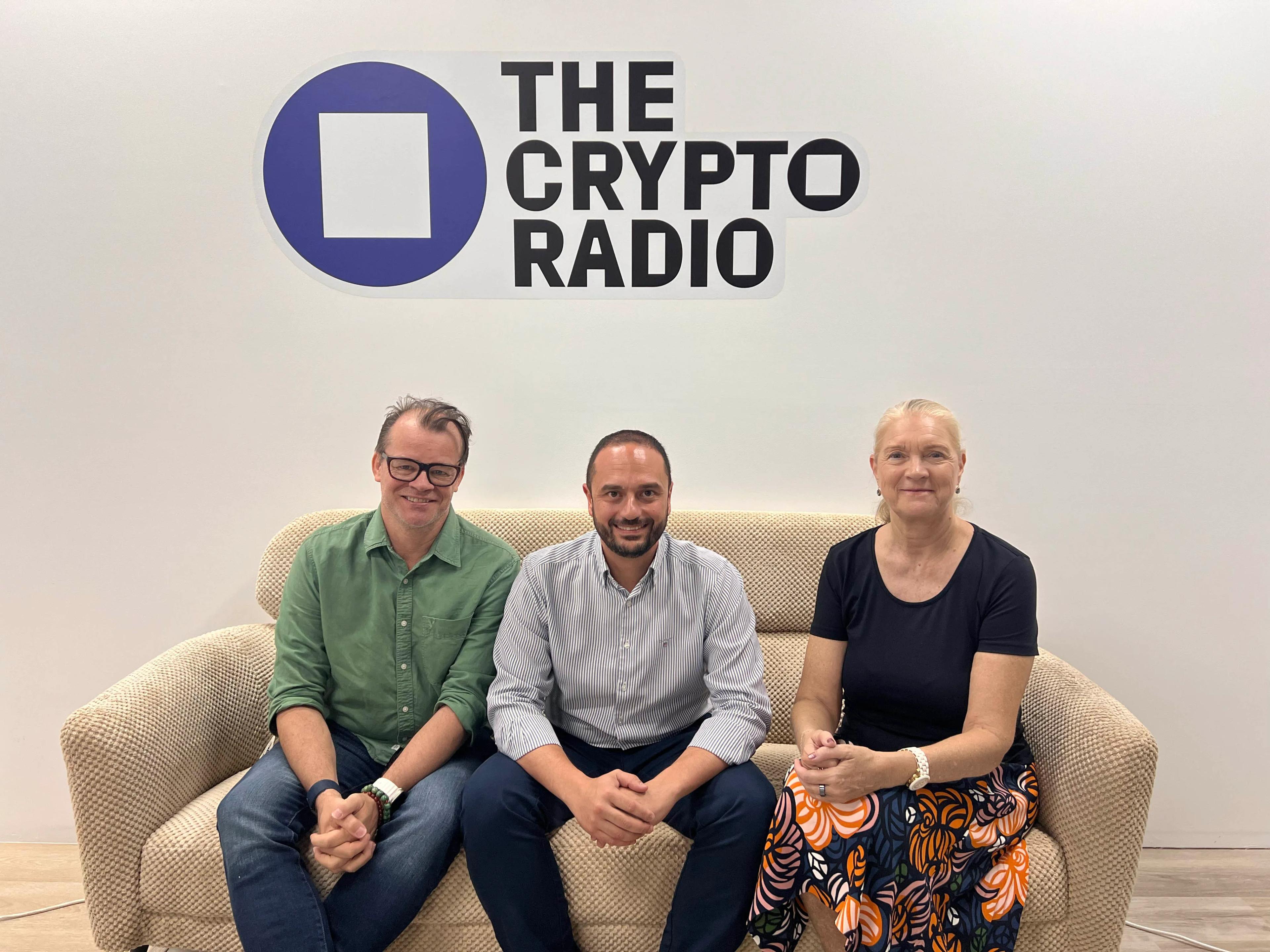 A photo of two men and one woman sitting on a sofa under a sign reading The Crypto Radio