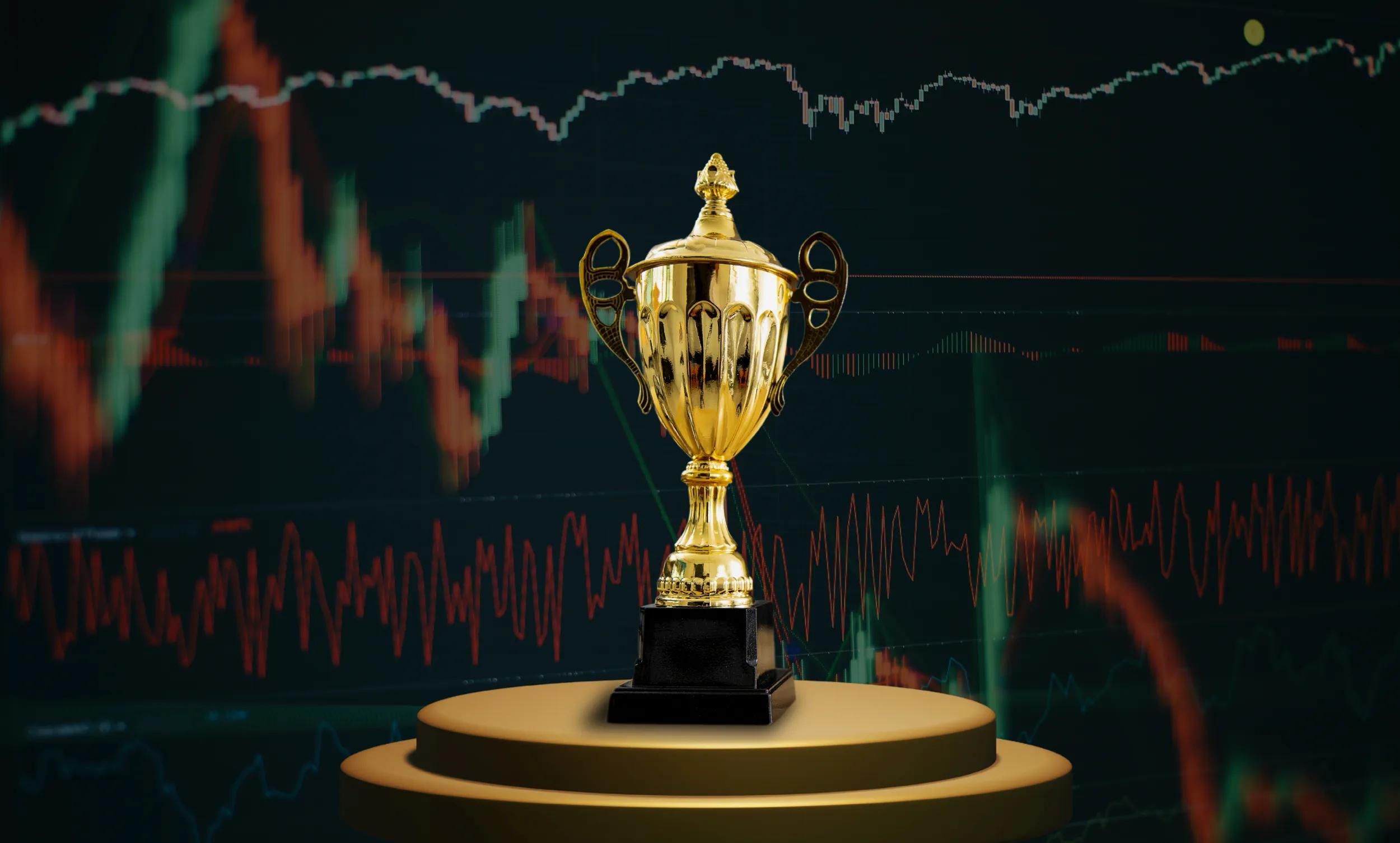 A trophy in front of a screen displaying price charts