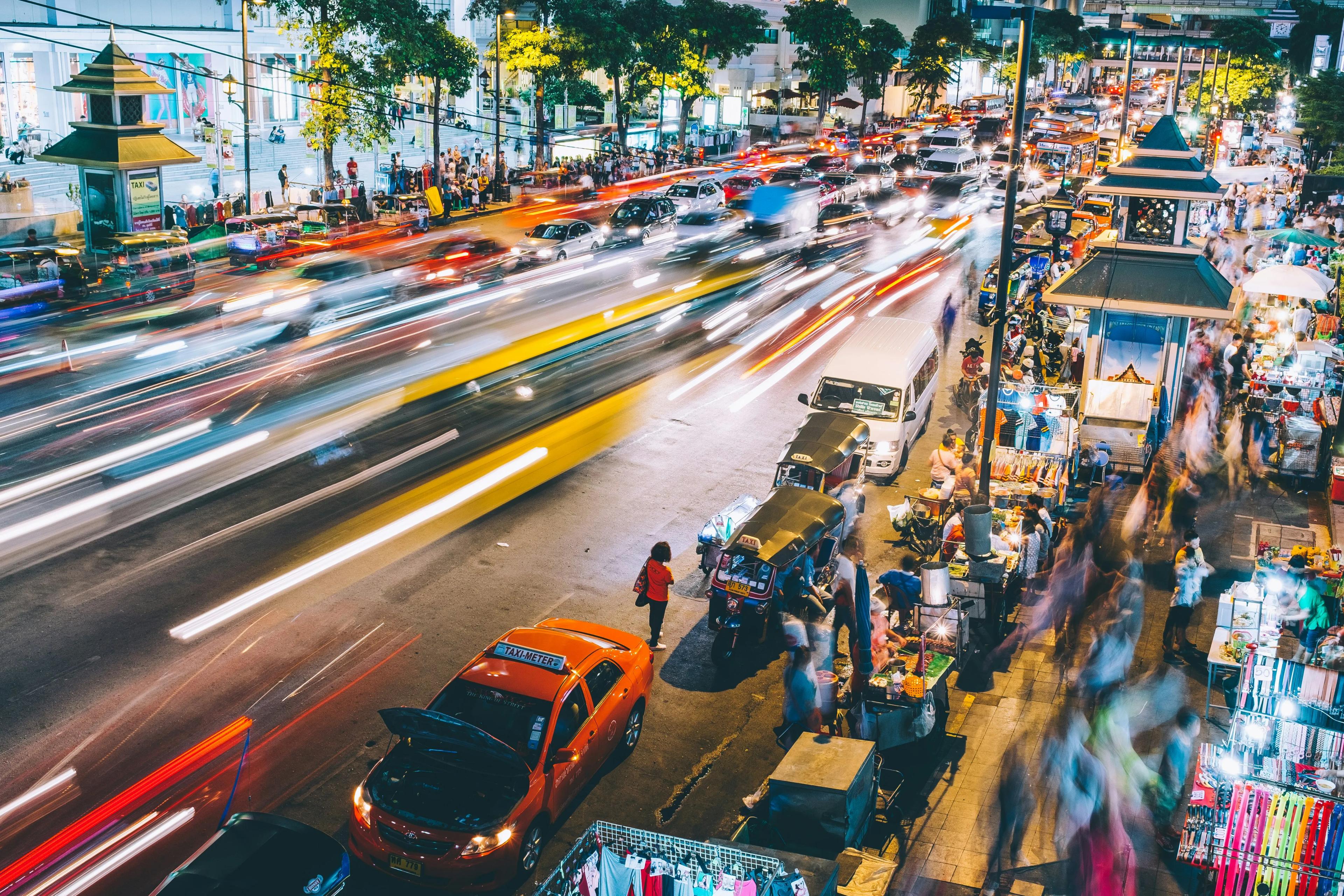 Bustling street in Bangkok with blurred traffic and pedestrians, capturing the city's energy and movement