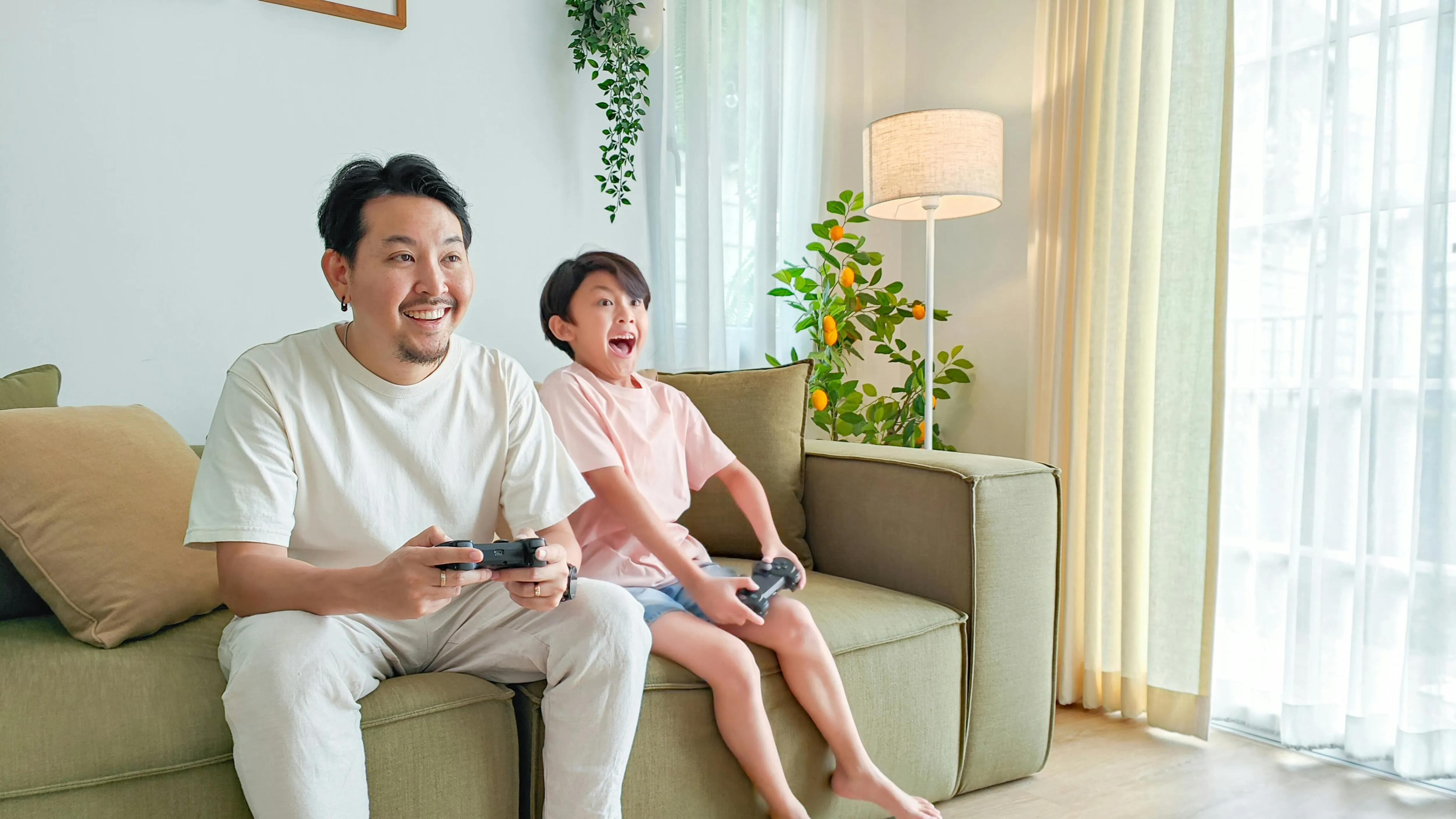 One man and one boy with gaming console controllers sitting on a sofa