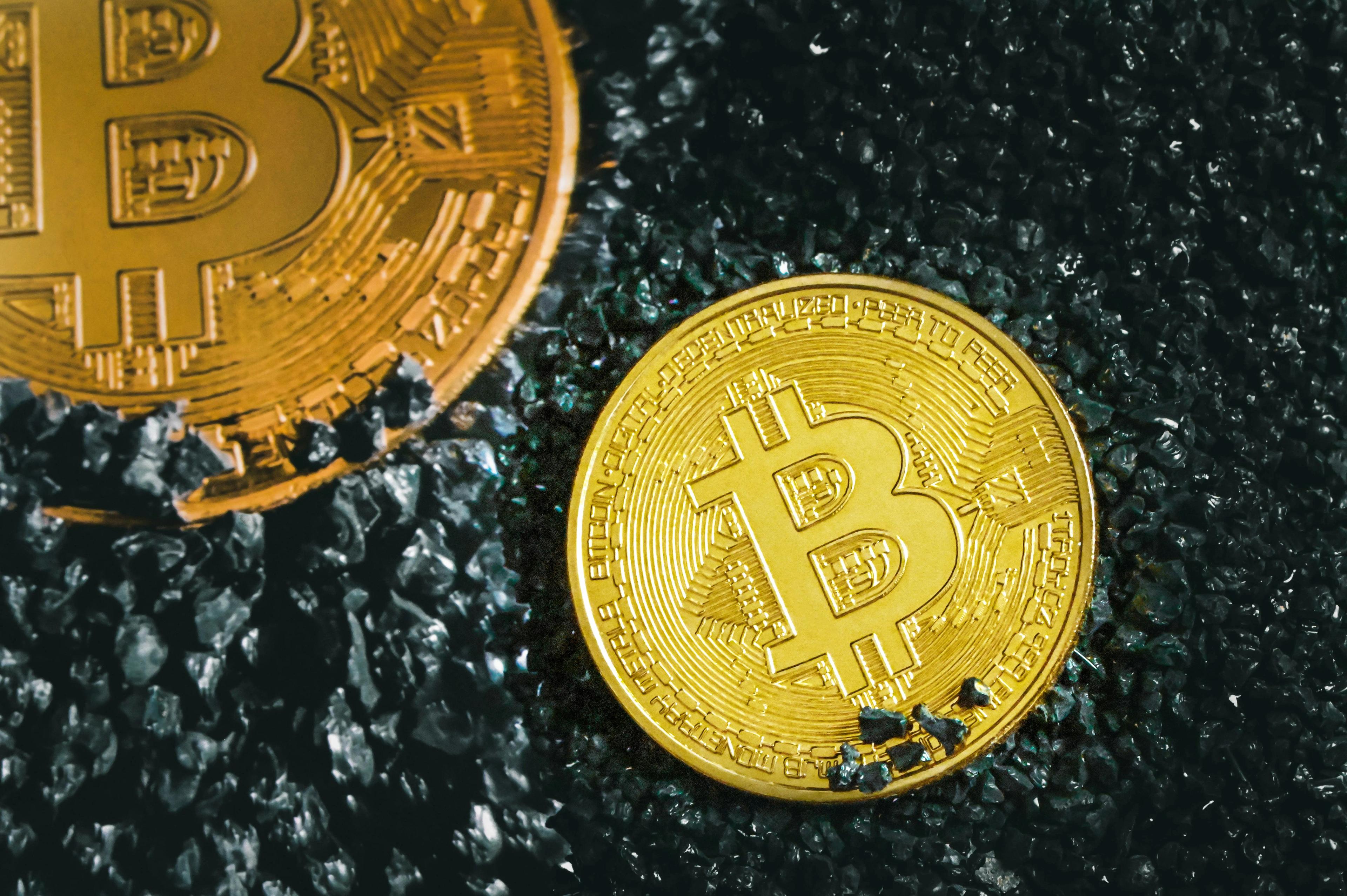Two Bitcoin coins sitting in black gravel